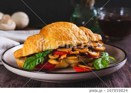 Appetizing croissant stuffed with fried champignons and tomatoes on a plate 107859824