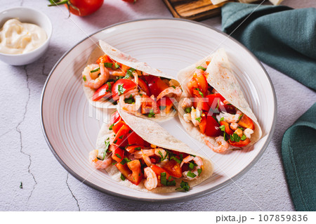 Soft appetizer mini tacos with shrimp, tomatoes and herbs on a plate 107859836