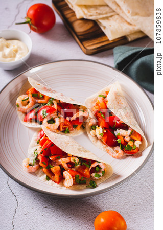 Soft appetizer mini tacos with shrimp, tomatoes and herbs on a plate vertical view Soft appetizer mini tacos with shrimp, tomatoes and herbs on a plate vertical view 107859838