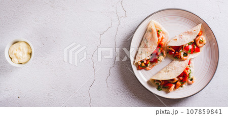 Soft appetizer mini tacos with shrimp, tomatoes and herbs on a plate top view web banner 107859841