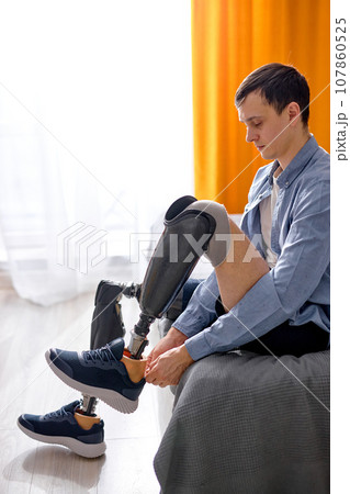rehabilitation after leg amputation, man getting used to prosthesis on legs, wearing sneakers rehabilitation after leg amputation, man getting used to prosthesis on legs, wearing sneakers 107860525