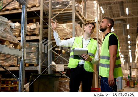 workers in uniform make an inventory management of products on shelves in warehouse 107860556