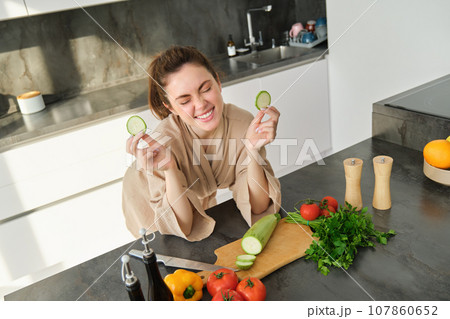 Portrait of beautiful brunette woman in the kitchen, wearing bathrobe, chopping vegetables on board, cooking healthy vegetarian food, preparing salad, making a meal Portrait of beautiful brunette woman in the kitchen, wearing bathrobe, chopping vegetables on board, cooking healthy vegetarian food, preparing salad, making a meal 107860652