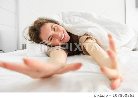 Cheerful girl stretching her arms in bed, waking up from good sleep or nap, enjoying the morning 107860863