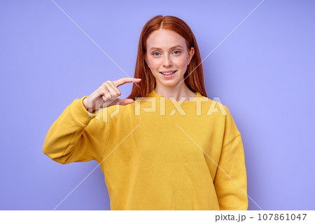 smiling cheerful red-haired girl gesturing with hand doing small size sign 107861047