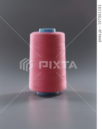 Thread for dressmaking, pink colour thread spool on grey surface, yarn for sewing 107861181