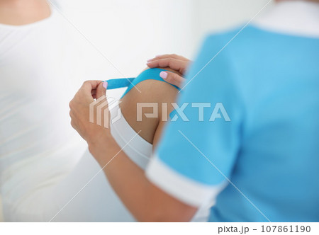 Physiotherapist put kinesiology tape on knee, injured part of patient body 107861190