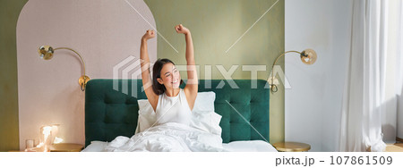 Portrait of smiling happy asian girl, wakes up feeling enthusiastic, stretches her hands up, enjoys good morning in her bedroom Portrait of smiling happy asian girl, wakes up feeling enthusiastic, stretches her hands up, enjoys good morning in her bedroom 107861509