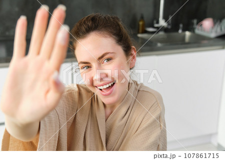 Attractive young cheerful girl baking at the kitchen, making dough, holding recipe book, having ideas 107861715