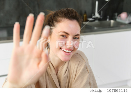 Attractive young cheerful girl baking at the kitchen, making dough, holding recipe book, having ideas 107862112