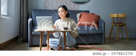 Portrait of young working woman, korean girl studying on remote online, talking to laptop, video chat, has conversation via computer application Portrait of young working woman, korean girl studying on remote online, talking to laptop, video chat, has conversation via computer application 107862259
