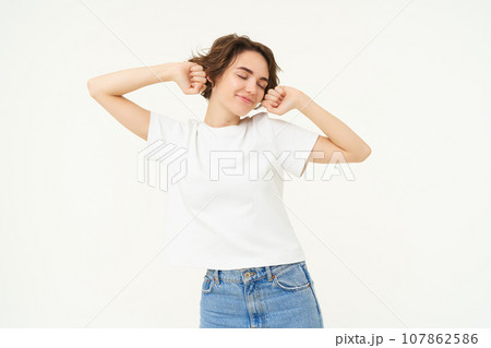 Portrait of smiling, pleased woman stretching hands, waking up after sleep, standing over white background 107862586