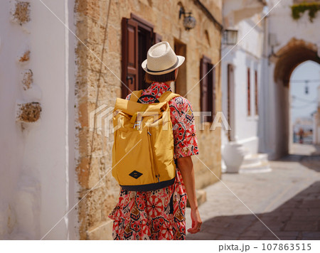 Nice asian Female in boho dress Enjoying Sunny Day on Greek Islands. Travel to Lindos, Mediterranean islands tourist season. Tourist woman on vacation in Greece walking through the streets of Lindos. Nice asian Female in boho dress Enjoying Sunny Day on Greek Islands. Travel to Lindos, Mediterranean islands tourist season. Tourist woman on vacation in Greece walking through the streets of Lindos. 107863515