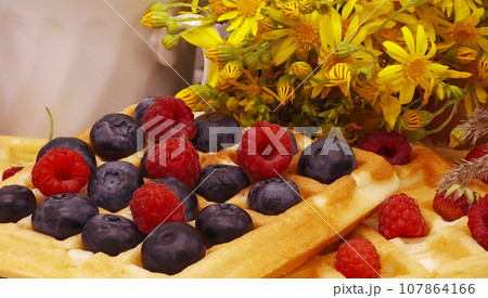 Viennese cookies with raspberries and blueberries. A bouquet of meadow flowers, a cup of tea or coffee. Morning summer breakfast. Side view. Close-up. Viennese cookies with raspberries and blueberries. A bouquet of meadow flowers, a cup of tea or coffee. Morning summer breakfast. Side view. Close-up. 107864166
