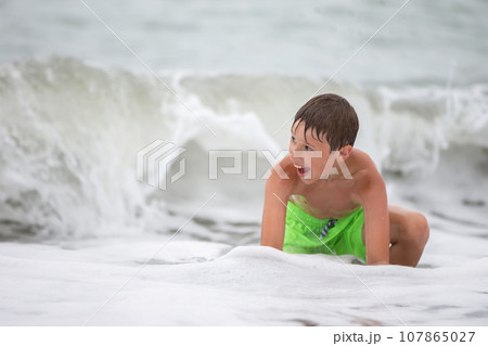 Happy boy bathes in the sea, plays with waves and splashes. Happy boy bathes in the sea, plays with waves and splashes. 107865027