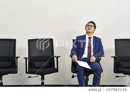 frustrated older asian man sitting in a chair frustrated older asian man sitting in a chair 107865234