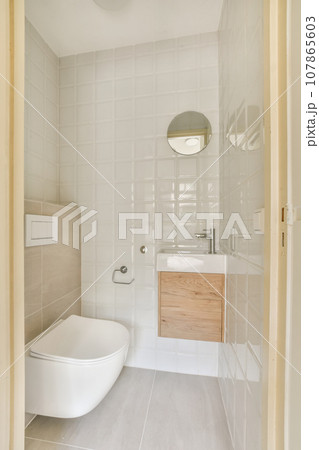 a small bathroom with white tiles and wood cabinet in the corner, as seen from the doorway leading to the toilet a small bathroom with white tiles and wood cabinet in the corner, as seen from the doorway leading to the toilet 107865603