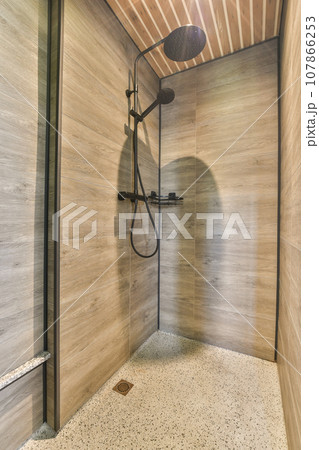 a shower room with wood walls and tile flooring on the wall, there is an open shower stall that has a hand held 107866253