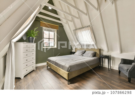 a bedroom with a bed, dresser and chair in the corner of an attic - style room that has been used for several years a bedroom with a bed, dresser and chair in the corner of an attic - style room that has been used for several years 107866298