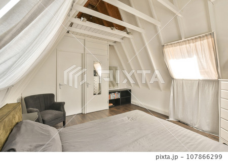 a bedroom with a bed, chair and window in the attic style room that has been used for many years 107866299