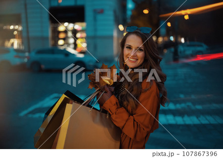 happy elegant female in orange trench coat with shopping bags 107867396