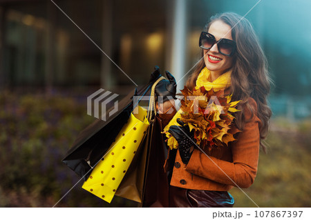 smiling modern female in orange trench coat with shopping bags 107867397