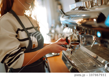 Female barista making coffee in a coffee machine. Conception of business and service. Takeaway food. Female barista making coffee in a coffee machine. Conception of business and service. Takeaway food. 107867931