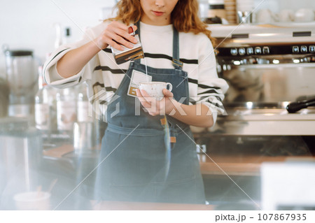 Female barista making coffee in a coffee machine. Conception of business and service. Takeaway food. Female barista making coffee in a coffee machine. Conception of business and service. Takeaway food. 107867935