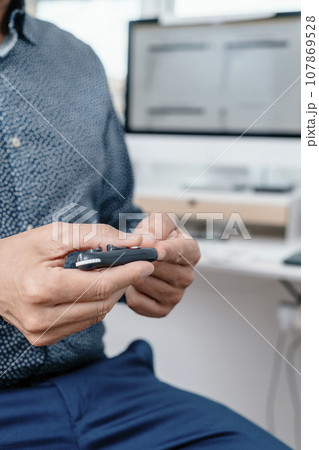 man pricking his finger with a fingerstick in the office man pricking his finger with a fingerstick in the office 107869528