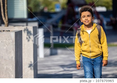 Curly-haired schoolboy with a backpack walking in the street Curly-haired schoolboy with a backpack walking in the street 107870965