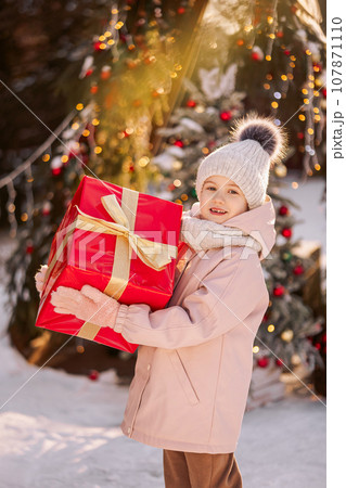 Little girl with a big Christmas gift outdoors in winter on Christmas Eve. Little girl with a big Christmas gift outdoors in winter on Christmas Eve. 107871110