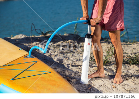 Unrecognizable man preparing yellow SUPboard for surfing. Unrecognizable man preparing yellow SUPboard for surfing. 107871366