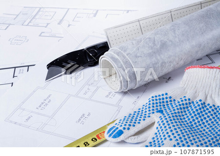 Laying flooring. Linoleum, a knife and a house plan on the builder's table. Taking measurements for laying the floor. Laying flooring. Linoleum, a knife and a house plan on the builder's table. Taking measurements for laying the floor. 107871595