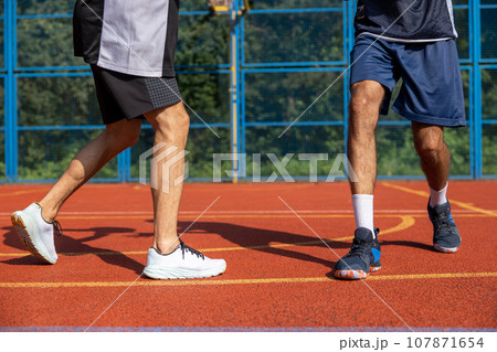Two unrecognizable men playing basketball in court outdoors. Two unrecognizable men playing basketball in court outdoors. 107871654