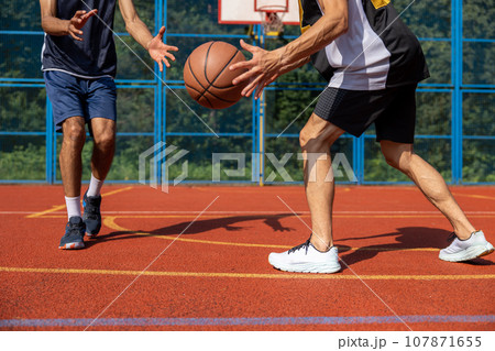 Two unrecognizable men playing basketball in court outdoors. Two unrecognizable men playing basketball in court outdoors. 107871655