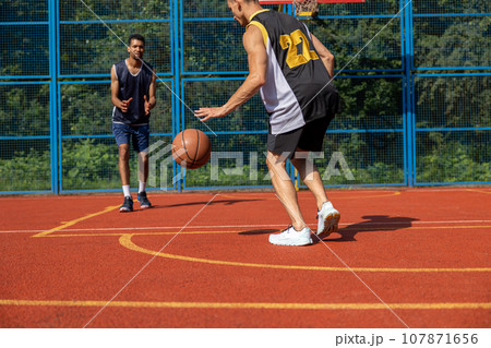Two unrecognizable men playing basketball in court outdoors. Two unrecognizable men playing basketball in court outdoors. 107871656
