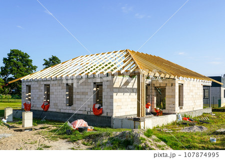 Unfinished residential house with white concrete block walls and a wooden beam truss roof structure Unfinished residential house with white concrete block walls and a wooden beam truss roof structure 107874995
