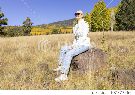 Happy Smiling Woman Takes A Rest During Hiking In Mountains At Fall Season On Bright Sunny Day. Young Smiling Female Hiker Does Sport , Trekking In Autumn Nature On Vacation. Travel, Active Lifestyle 107877266
