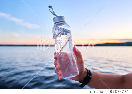 A man holds a bottle of water against the backdrop of a lake. A man holds a bottle of water against the backdrop of a lake. 107878774