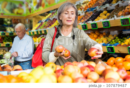 Mature lady choosing fresh apples in greengrocer Mature lady choosing fresh apples in greengrocer 107879487