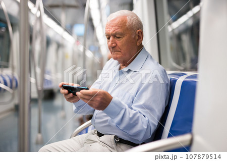 Old man with smartphone sitting inside subway train 107879514
