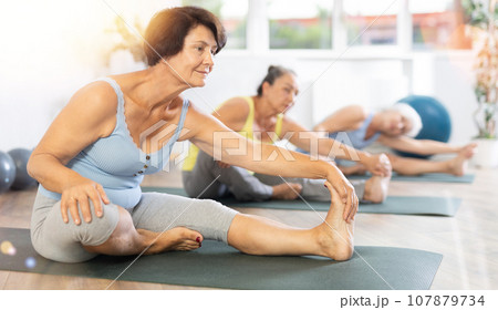 Mature lady performs Janu shirshasana 107879734