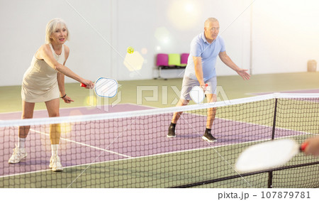 Athletic seniors playing pickleball on court indoors 107879781