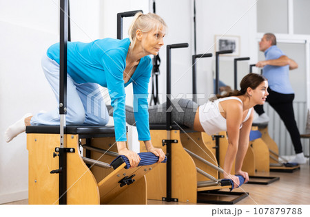 Focused mature woman performing stretching exercises while using pilates Wanda chair machine in fitness center 107879788