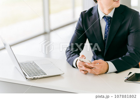 パソコンをスマホを両方使う若いアジア人ビジネスマン 107881802
