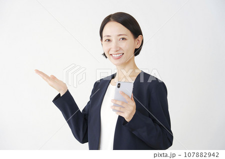 スマートフォンを持って左側を手のひらで指すビジネスウーマン　白背景 107882942