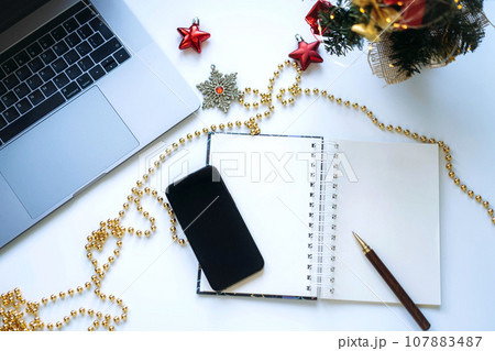open notepad with blank sheet for new year resolutions. laptop and christmas tree nearby open notepad with blank sheet for new year resolutions. laptop and christmas tree nearby 107883487