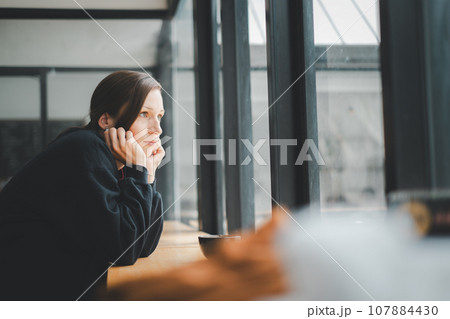 Sad woman sitting by the window looking outside Sad woman sitting by the window looking outside 107884430
