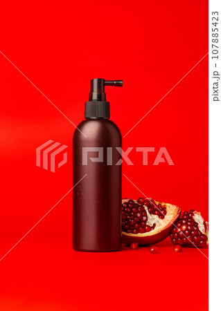 Cosmetic spray bottle with slices of pomegranate on red background Cosmetic spray bottle with slices of pomegranate on red background 107885423