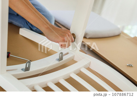 Man assembling white chair furniture at home 107886712